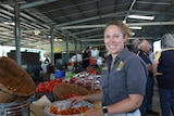 A woman smiles in a large shed in front of a basket of tomatoes.
