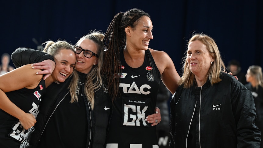 A coach and players of a Super Netball team hug and smile after a win in the team's final game.