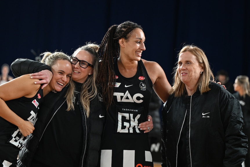 A coach and players of a Super Netball team hug and smile after a win in the team's final game.