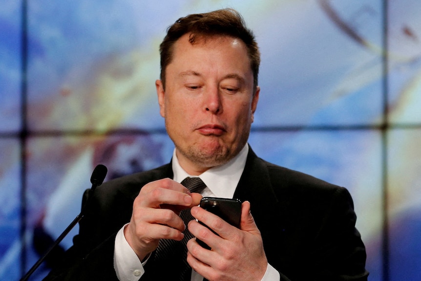 Elon Musk looks down at his smartphone.