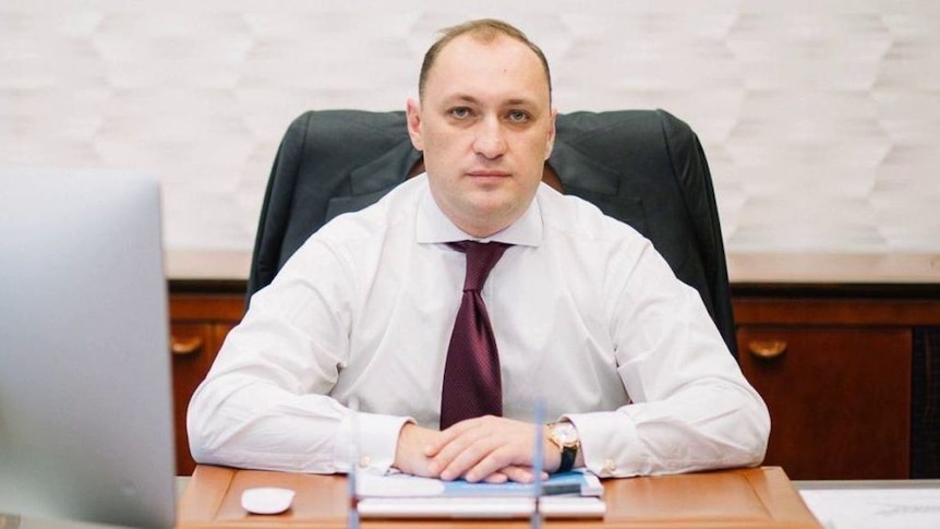 A man in a tie sits at a desk