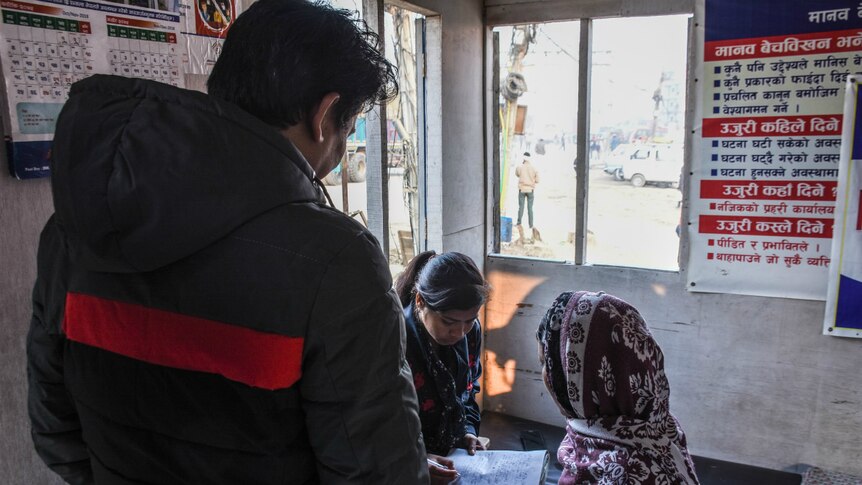 A woman writes on a notepad as she interviews another woman at the Nepal-India border.