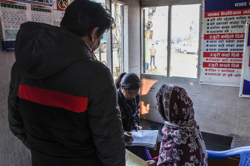 A woman writes on a notepad as she interviews another woman at the Nepal-India border.