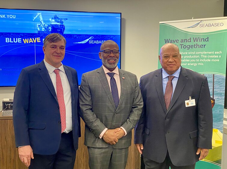 Three men standing shoulder to shoulder in suits smiling after singing an MoU for a wave technology in Tonga