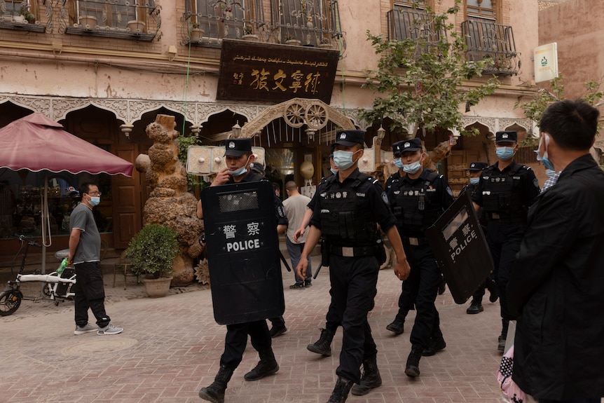 Chinese police officers with shields and batons patrol the streets of Xinjiang in May.