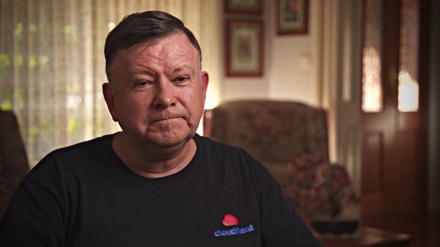 Man wearing a black shirt sitting in a living room.