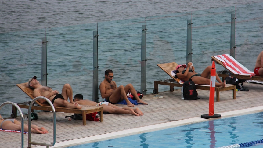 Swimmers sunbake on chairs around the pool at Andrew Boy Charlton pool on Sydney's Domain