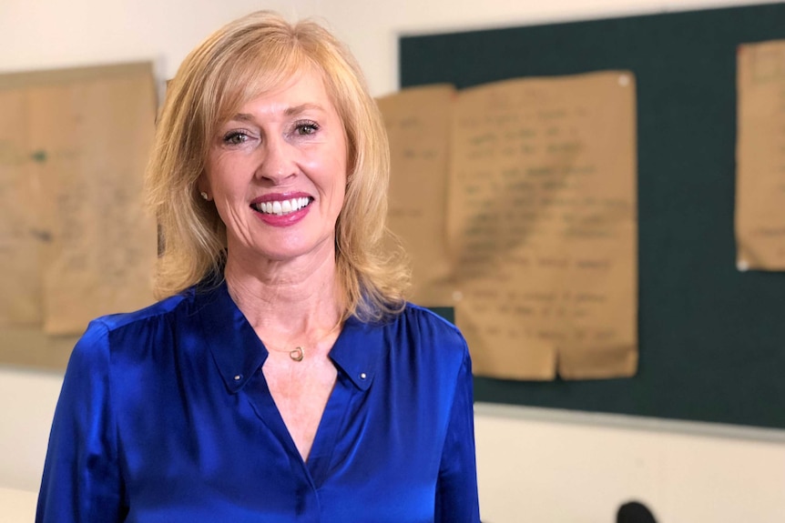 Kerry Uren smiles at the camera in a blue, shiny blouse against an out of focus background.