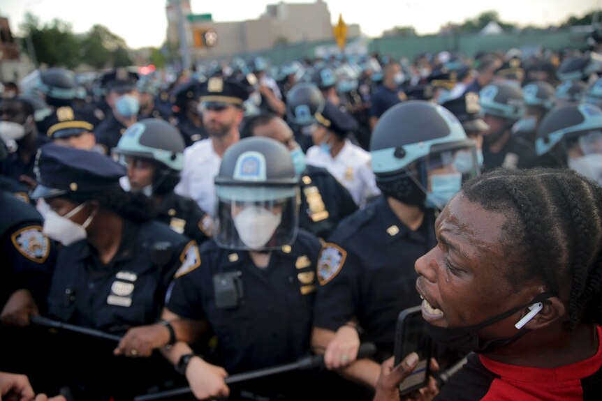A man stands to the right and cries in what appears to be distress as hundreds of police officers are seen in front.
