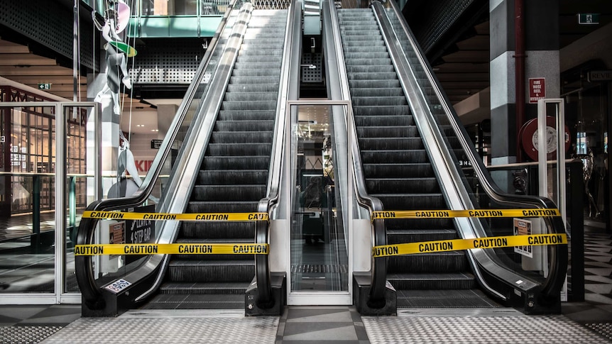 Two escalators are blocked by yellow tape in an empty shopping centre.