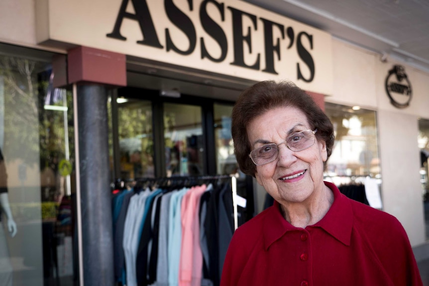 An elderly woman standing in front of a retail store.