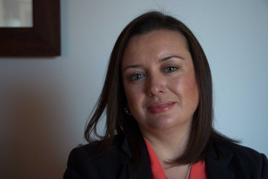 A 39-year-old woman with brown hair and blue eyes, wearing corporate clothes.