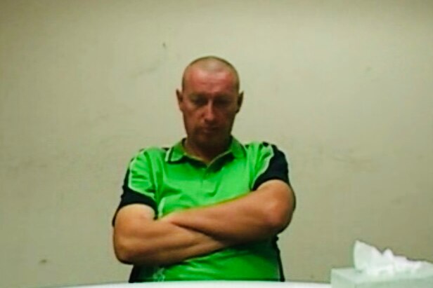 Peter John van de Wetering in police interview in 2014 sitting at table wit arms folded