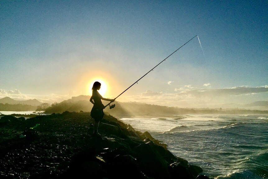 boy fishing at beach during a sunset