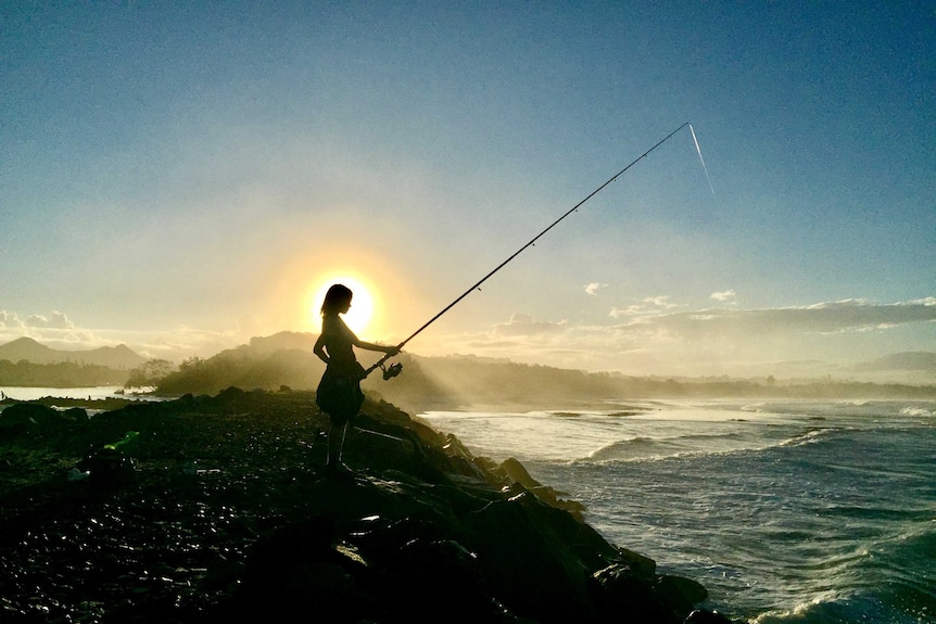 boy fishing at beach during a sunset