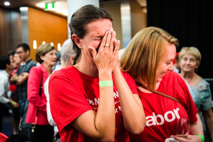 a woman crying and wiping her face at a labor party meeting waiting for election results