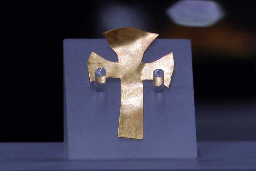 A gold foil cross mounted at a museum.