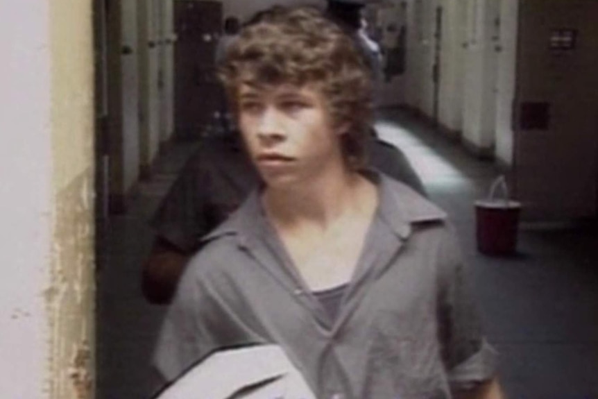 A young man in grey prisonwear carrying a box