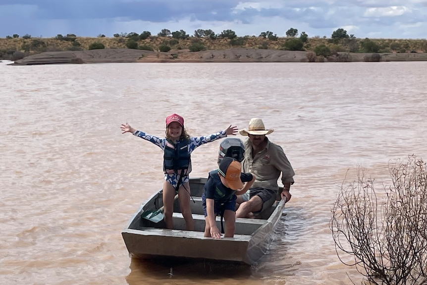 Two young children in a small boat with their father on a small dam