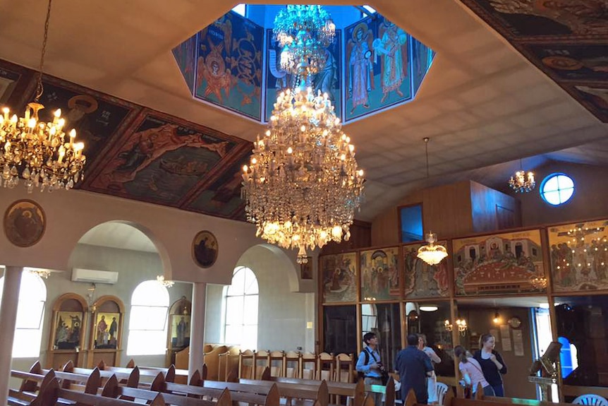 A large glass chandelier hanging over wooden pews in an ornate Greek Orthodox church