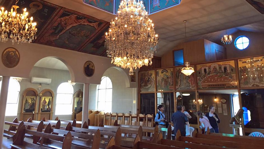 A large glass chandelier hanging over wooden pews in an ornate Greek Orthodox church