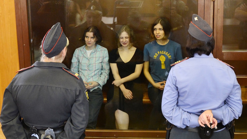 Pussy Riot members sit in a glass-walled cage during a court hearing in Moscow.