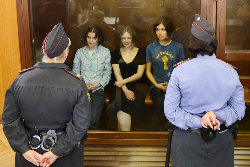 Pussy Riot members sit in a glass-walled cage during a court hearing in Moscow.