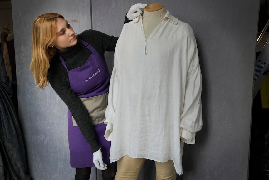 a woman wiht red hair in black clothes and clothes arranges the white shirt on a manequin
