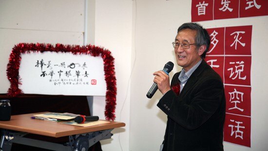 Haoliang Sun, holding a microphone, is standing in front of some Chinese characters stuck on a white wall in a room.