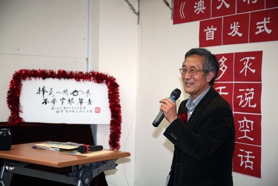 Haoliang Sun, holding a microphone, is standing in front of some Chinese characters stuck on a white wall in a room.