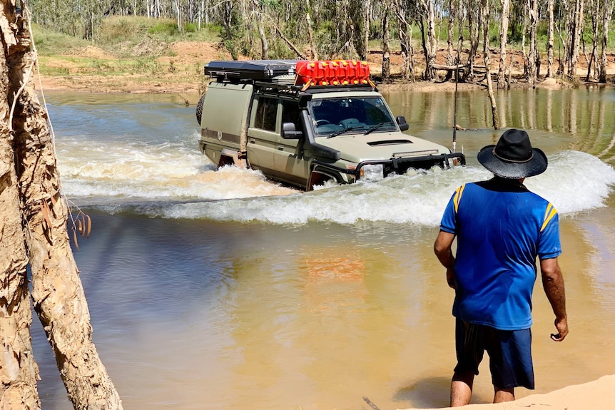 A man guides a four-wheel drive over a waterway.