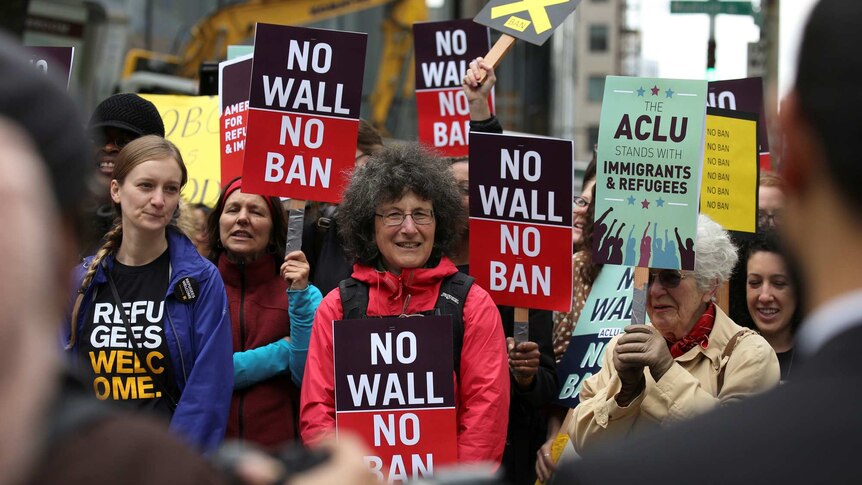 Protesters hold signs reading "No wall no ban"