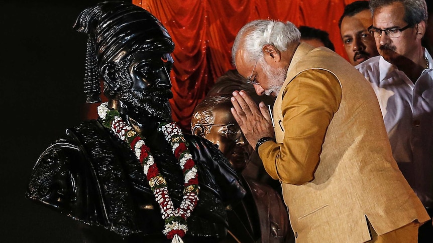 Narendra Modi bows his head to a statue of Shivaji with his hands in a prayer position.