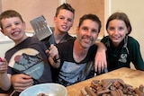 A man and his three children in their kitchen, smiling.