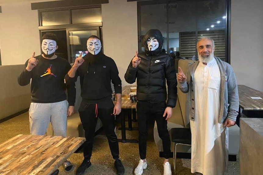 A man standing with three other man wearing masks to disguise their identity.