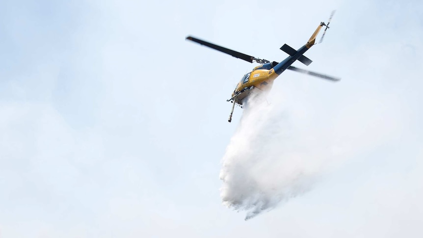 Waterbombing helicopter drops water on fire.