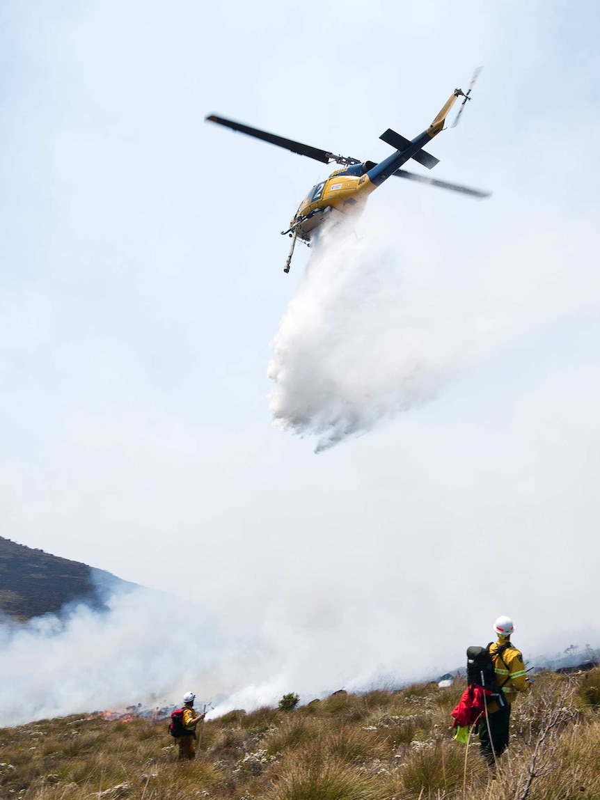 Waterbombing helicopter drops water on fire.