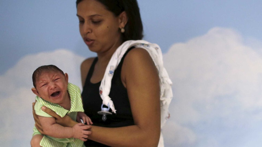 A mother holds a baby crying, who suffers from microephaly