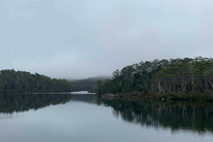 A picturesque lake on a cloudy day. The far horizon is slightly obscured by fog, but trees are visible closer to the forefront