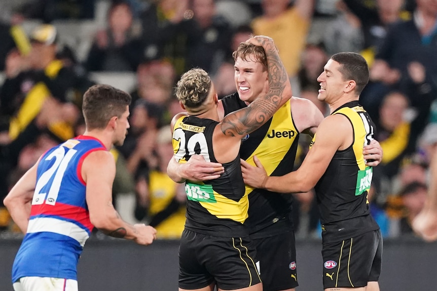 A star AFL forward is hugged by teammates after kicking a goal during a game. 