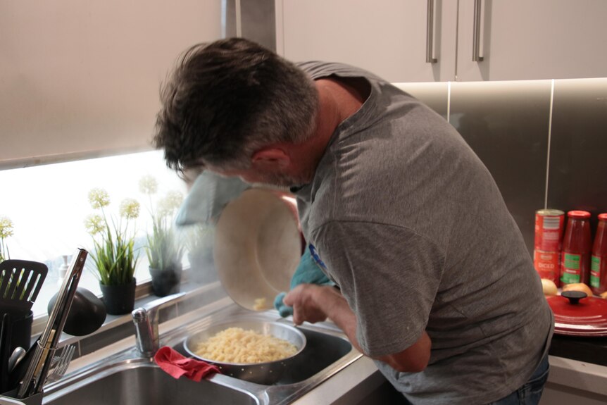 man pours pasta into a strainer 
