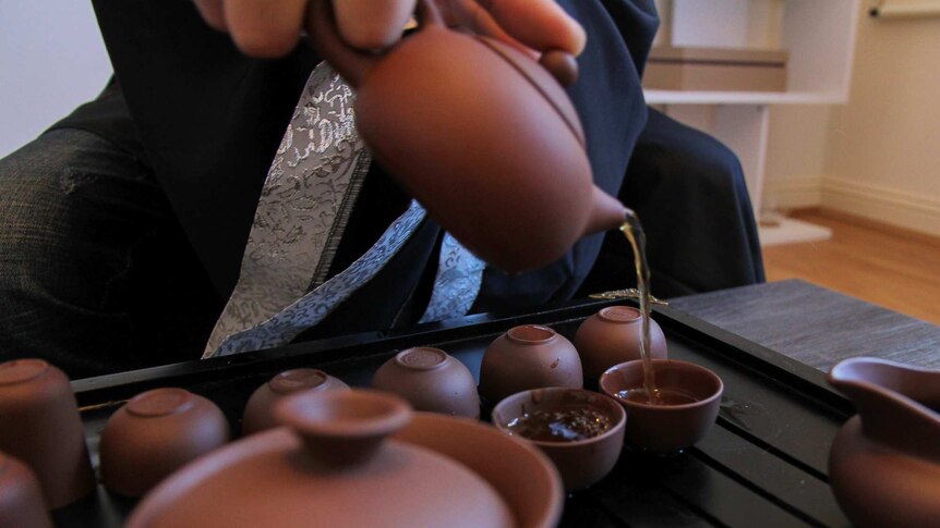 Close up of a teapot pouring tea into small brown chinese-style cups
