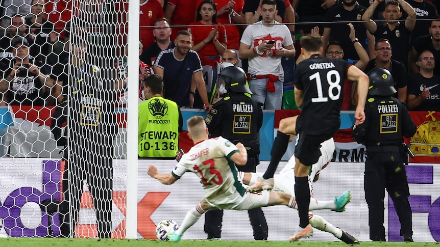 A German footballer swings his foot through the ball as a defender fails with an attempt to stop it hitting the net.