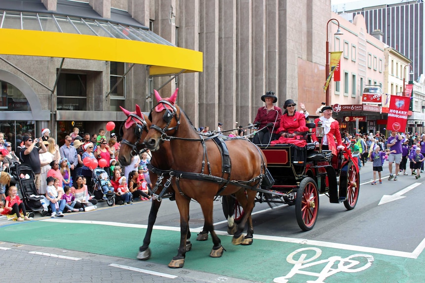 Une calèche avec des chevaux portant une casquette rouge sur les oreilles, une femme en rouge, deux hommes en vêtements victoriens, une plume en casquette, un costume.