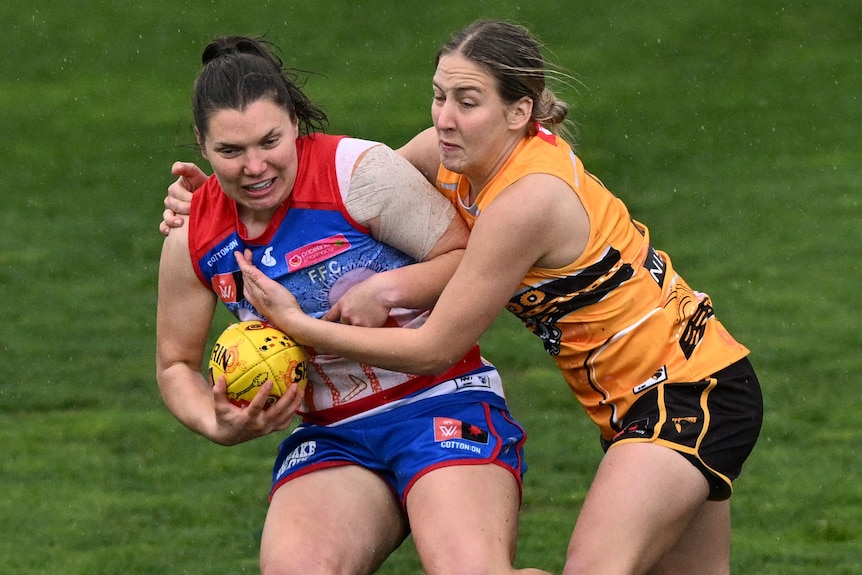 A Western Bulldogs AFLW player holds the ball while a Hawthorn opponent attempts a tackle.