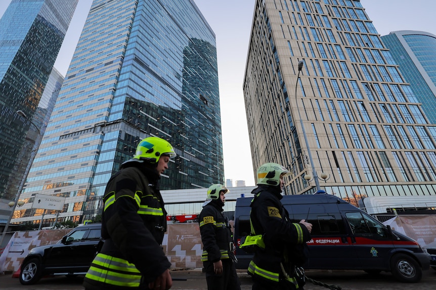 Firemen in yellow hi-vis stand in front of skyscrapers 