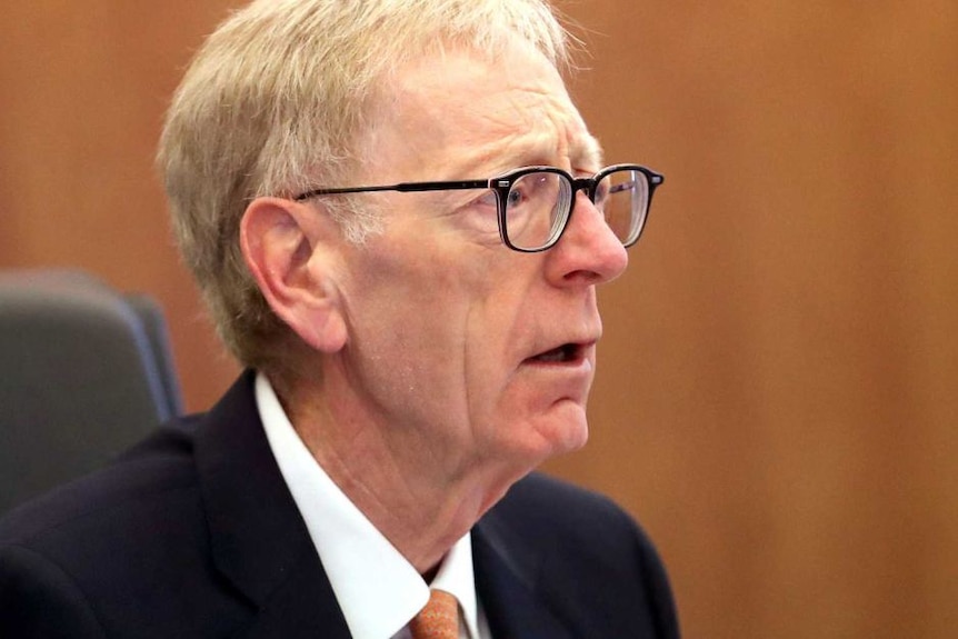 A man with a concerned look on his face, sitting at a judicial bench.