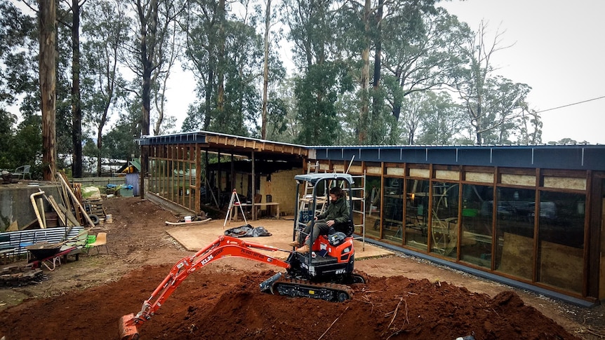 The Kinglake earthship with a person on a digger in the foreground.