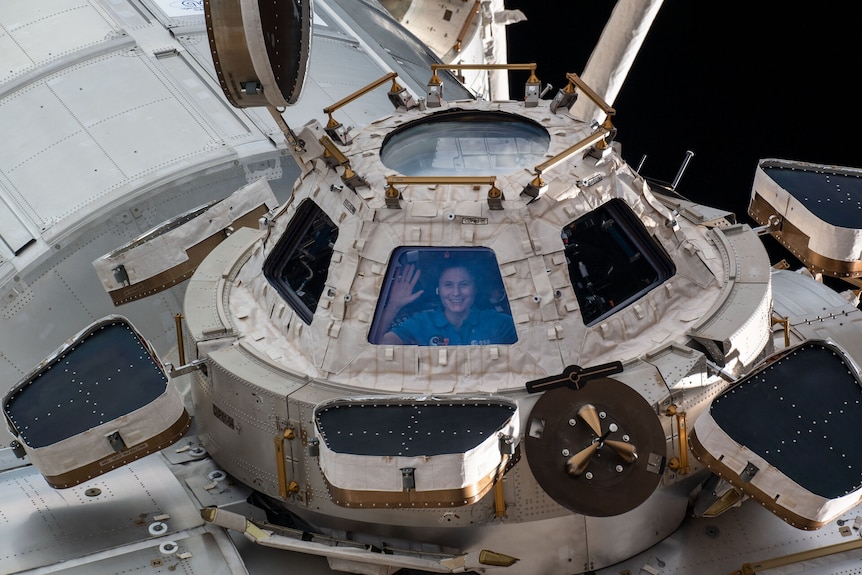 A woman inside the space station looking out a window with her hands against the glass