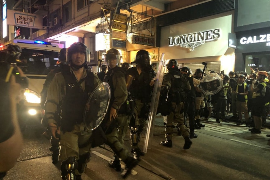 Lines of police with riot shields in street outside expensive shops.